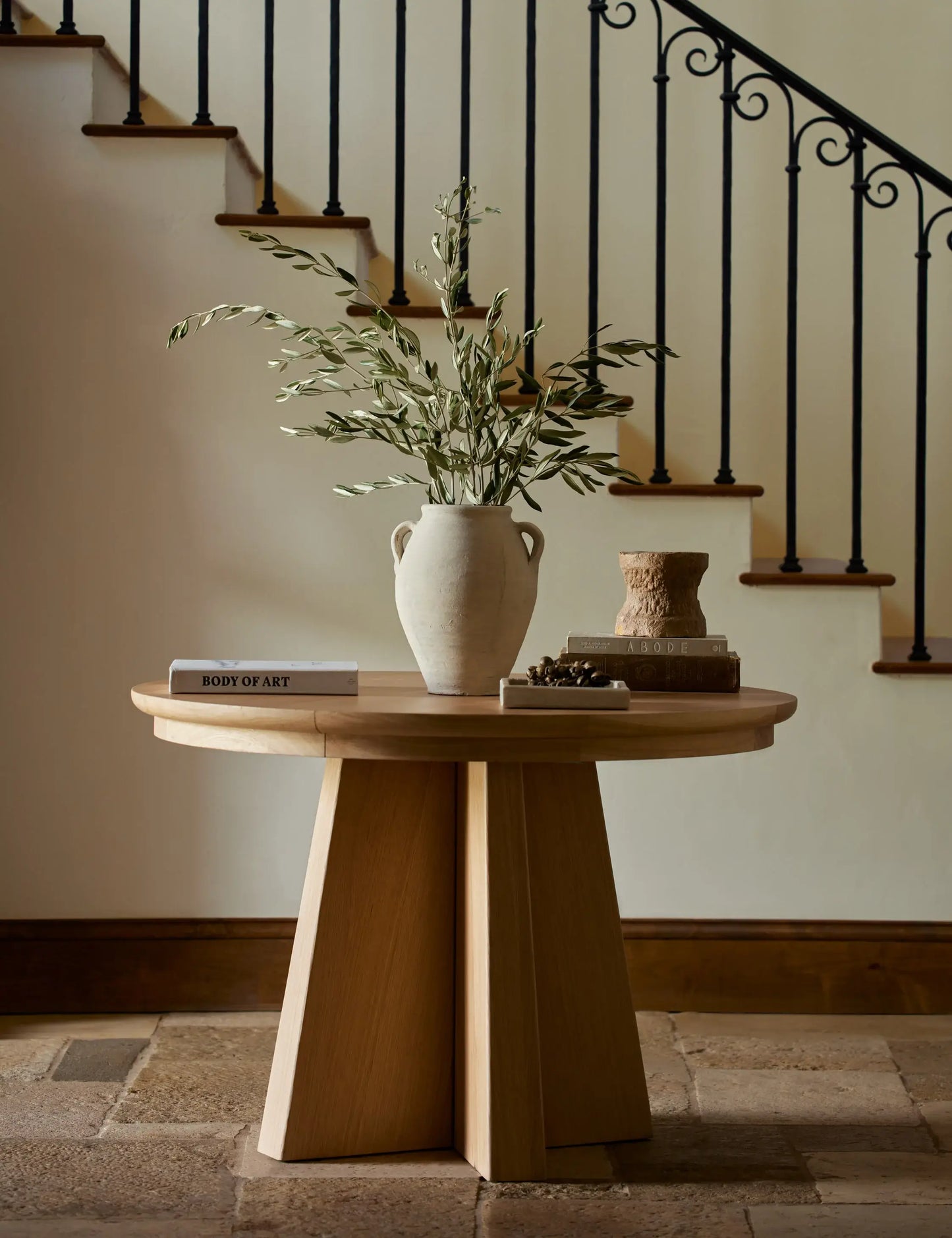 Ghareeb Extendable Oval Dining Table غريب styled in an elegant entryway with natural oak wood finish, modern sculptural base, and minimalist decor.