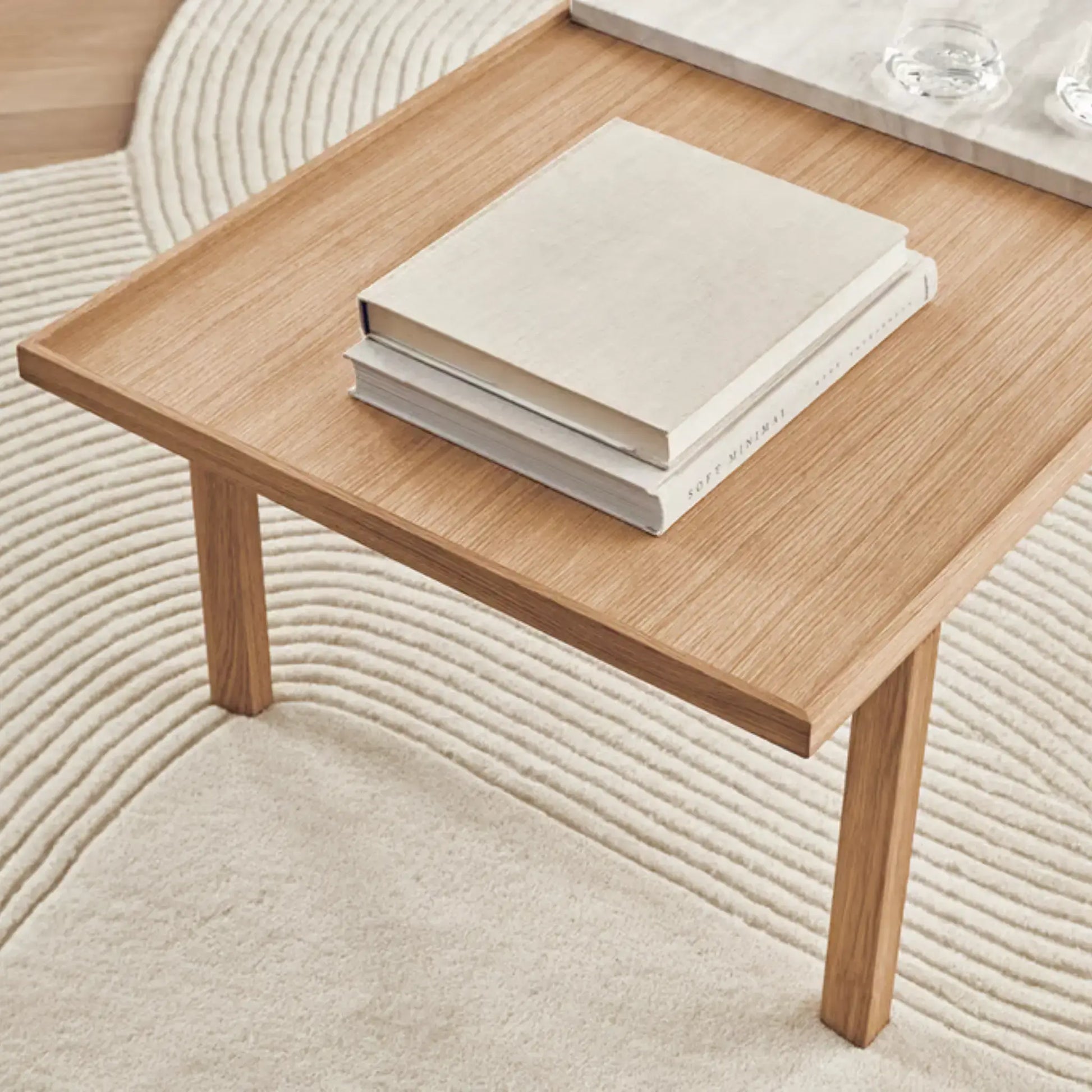 Oak Raha Table holding neutral-toned books on a textured ivory rug